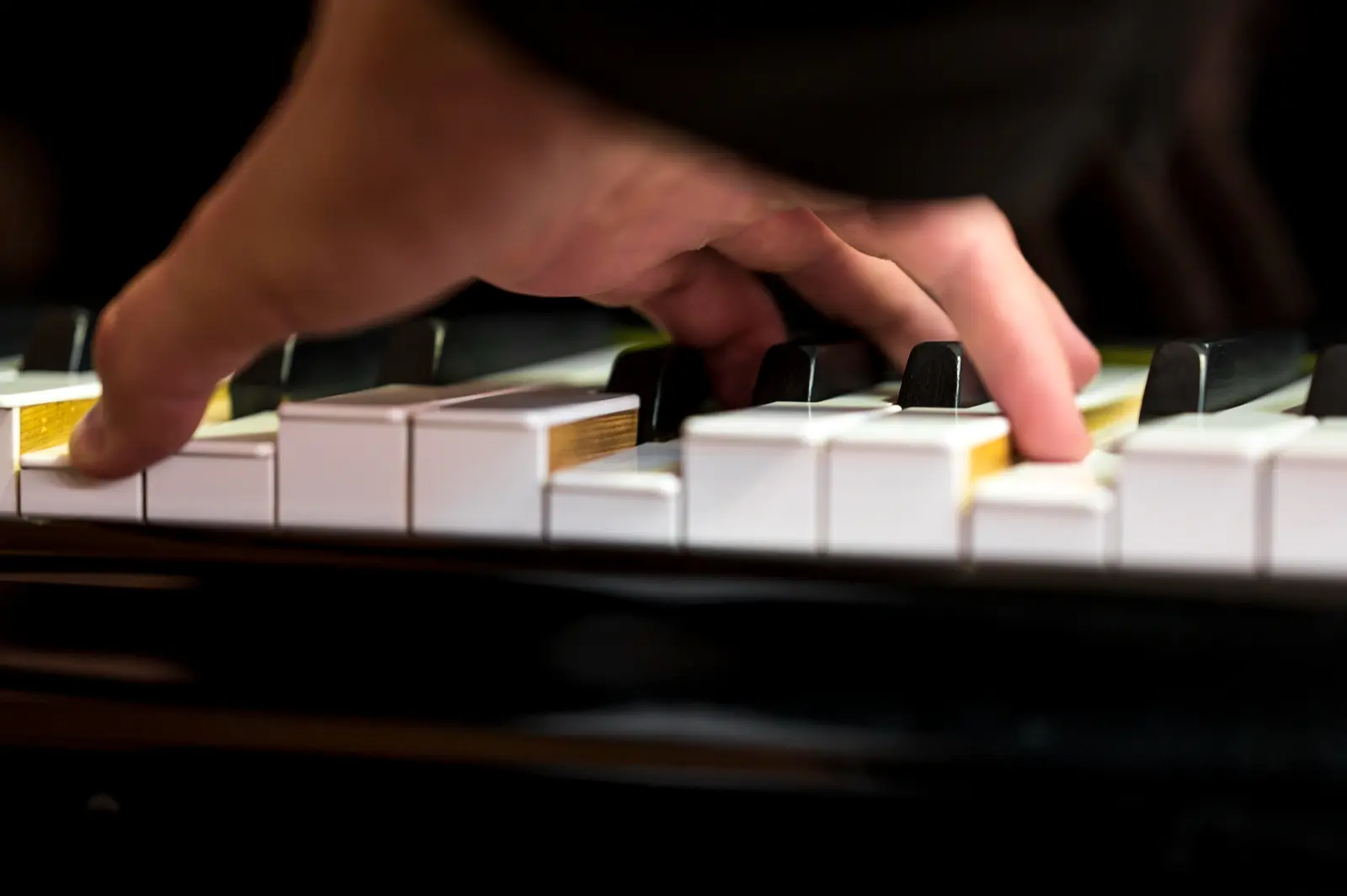 Mão sobre o teclado de um piano acústico, com o mecanismo dourado à vista